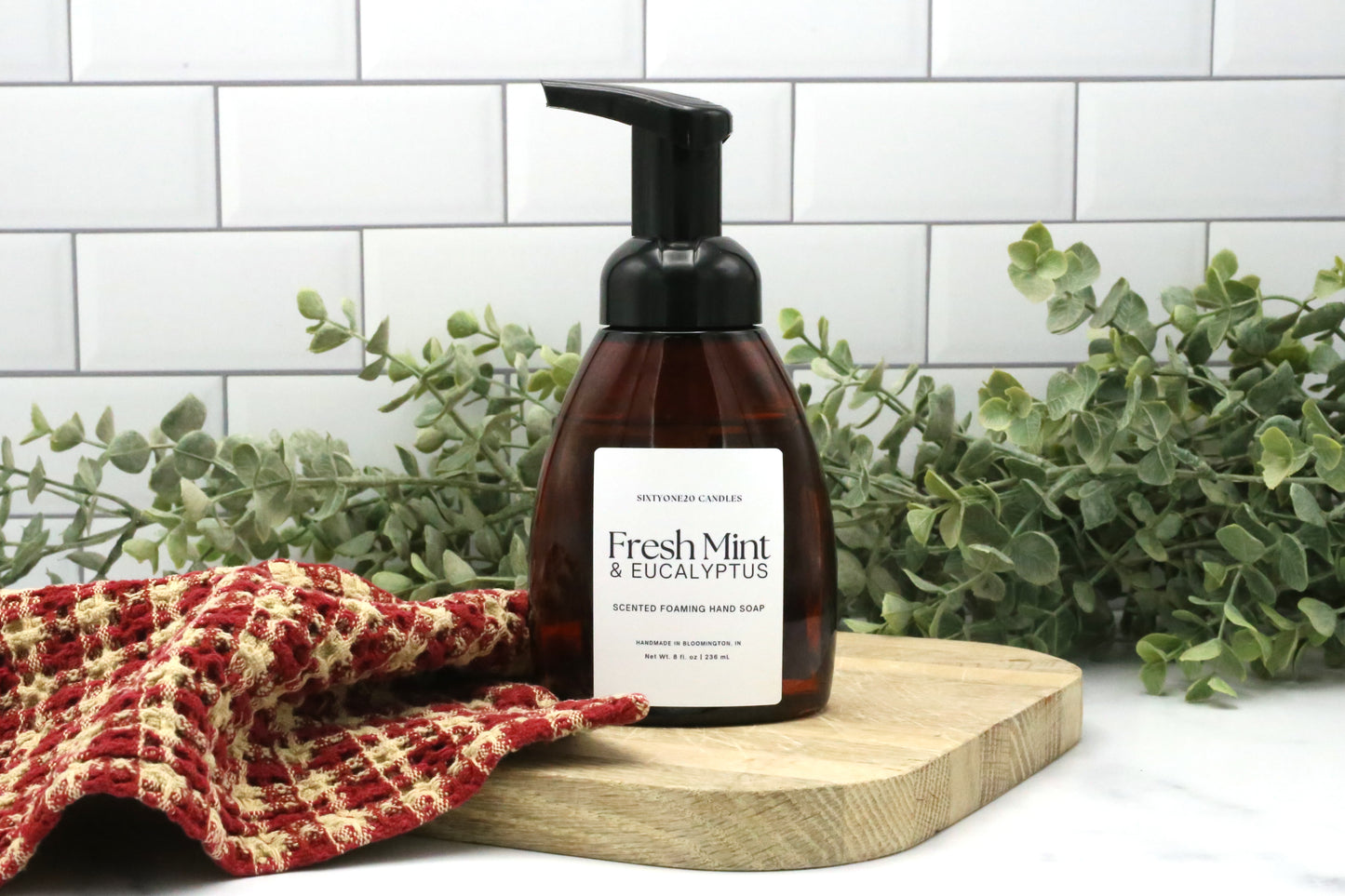 Fresh Mint and Eucalyptus foaming hand soap by Sixtyone20 Candles on a wooden board with red towel and greenery in the background