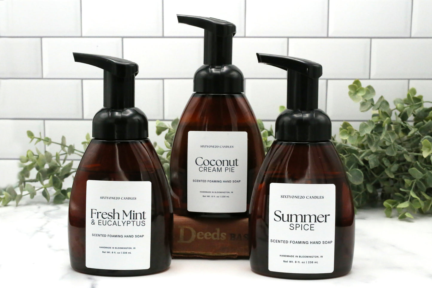 Three Sixtyone20 Candles foaming hand soaps in Fresh Mint and Eucalyptus, Coconut Cream Pie, and Summer Spice scents with a white tile and greenery backdrop