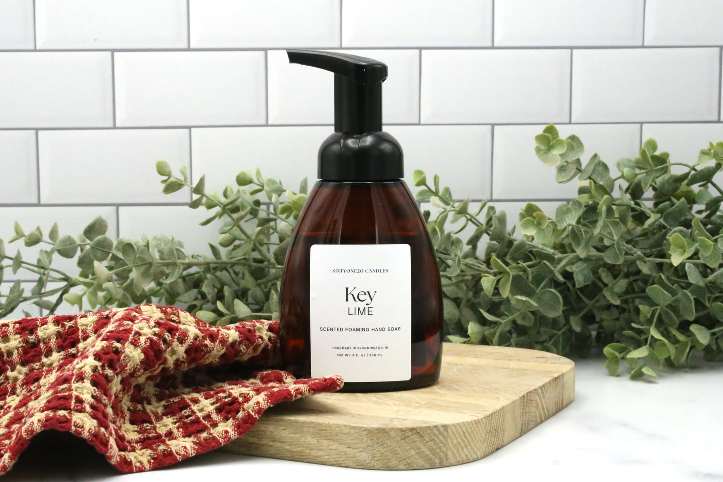 Key Lime foaming hand soap by Sixtyone20 Candles on a wooden board with red towel and eucalyptus greenery in the background