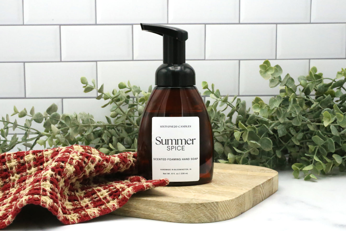 Summer Spice foaming hand soap by Sixtyone20 Candles on a wooden board with red towel and eucalyptus background