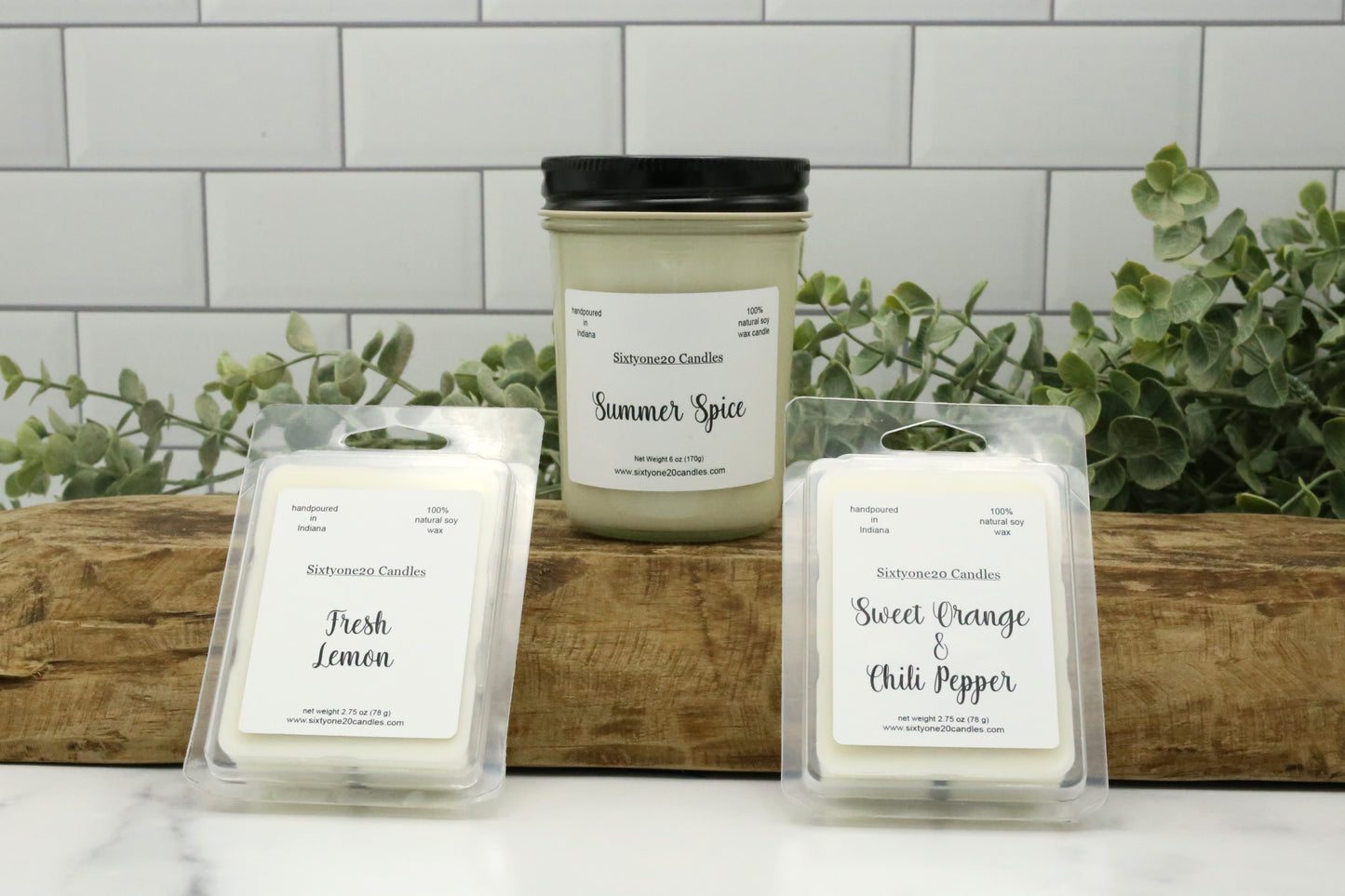 Summer Spice candle with Fresh Lemon and Sweet Orange & Chili Pepper wax melts from Sixtyone20 Candles, displayed on a wood slab with greenery in the background.