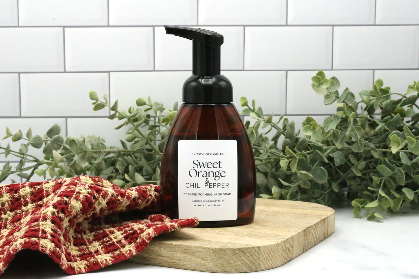 Sweet Orange and Chili Pepper foaming hand soap by Sixtyone20 Candles on a wooden board with red towel and greenery