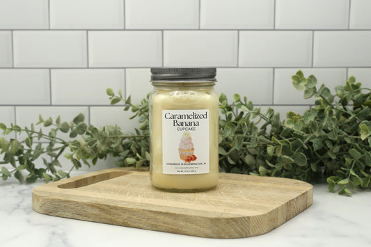 Caramelized Banana Cupcake Summer 2026 Candle Club candle in a 16 oz mason jar with silver lid on a wooden board