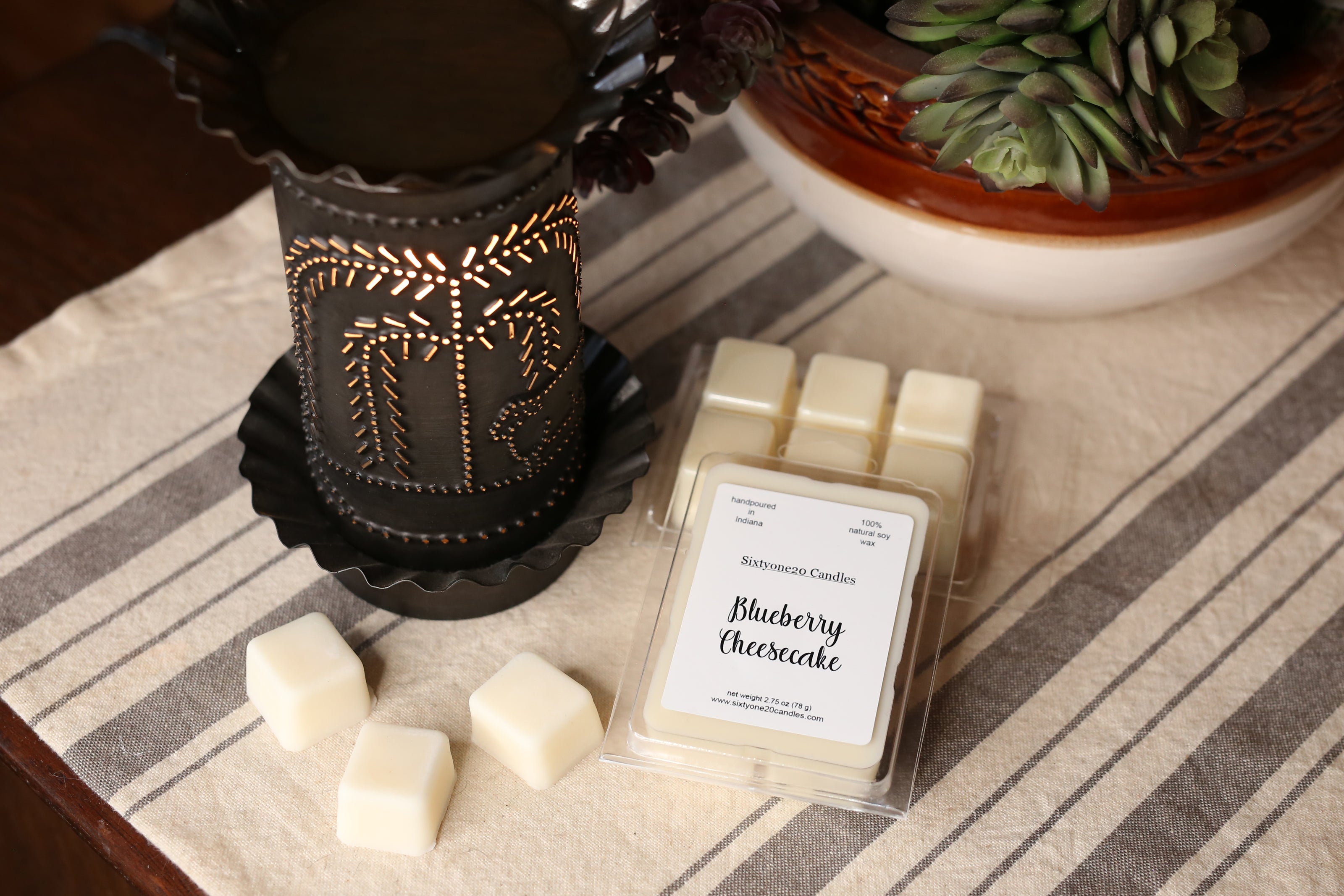 Scented wax melts with packaging labeled 'Blueberry Cheesecake' on a striped fabric surface.