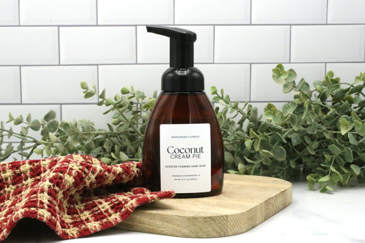 Coconut Cream Pie foaming hand soap by Sixtyone20 Candles displayed on a wooden board with red kitchen towel and greenery background