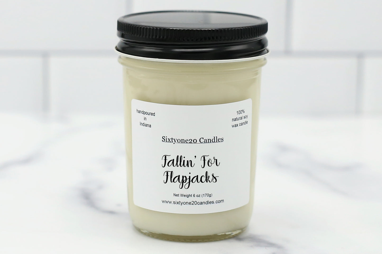 Fallin’ for Flapjacks soy candle in a clear glass jar with black lid, labeled and displayed on a white tile background