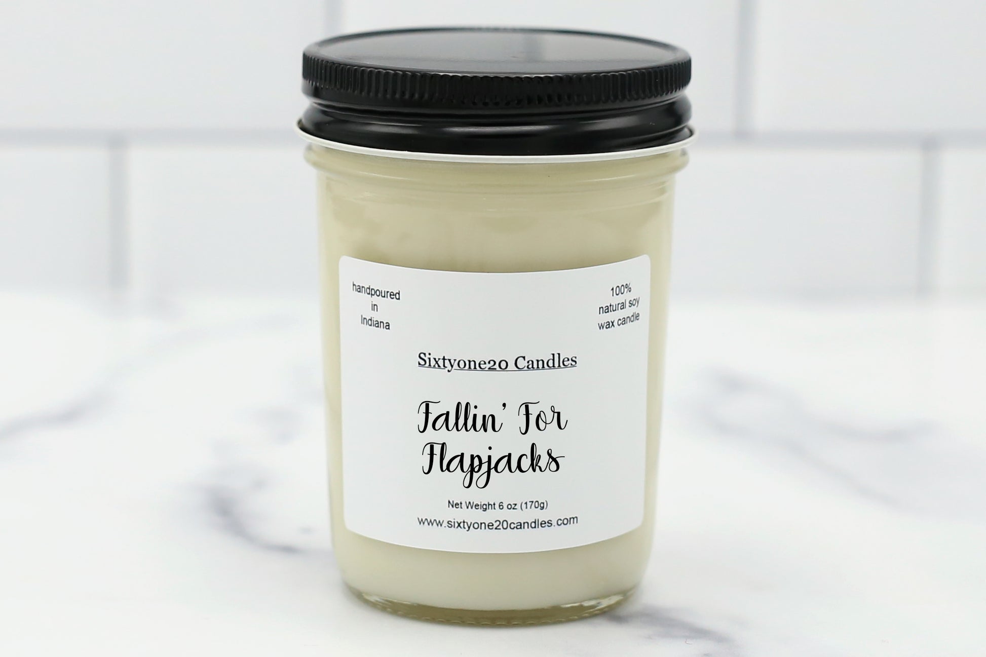 Fallin’ for Flapjacks soy candle in a clear glass jar with black lid, labeled and displayed on a white tile background