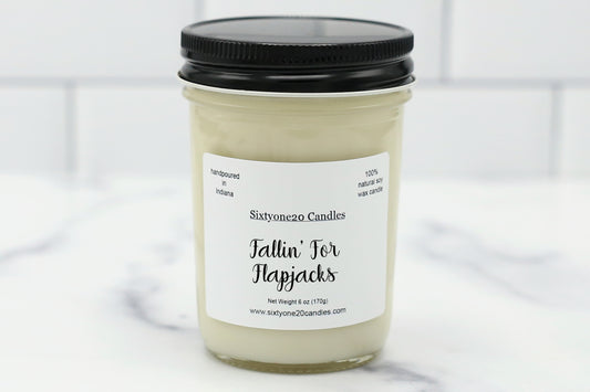 Fallin’ for Flapjacks soy candle in a clear glass jar with black lid, labeled and displayed on a white tile background