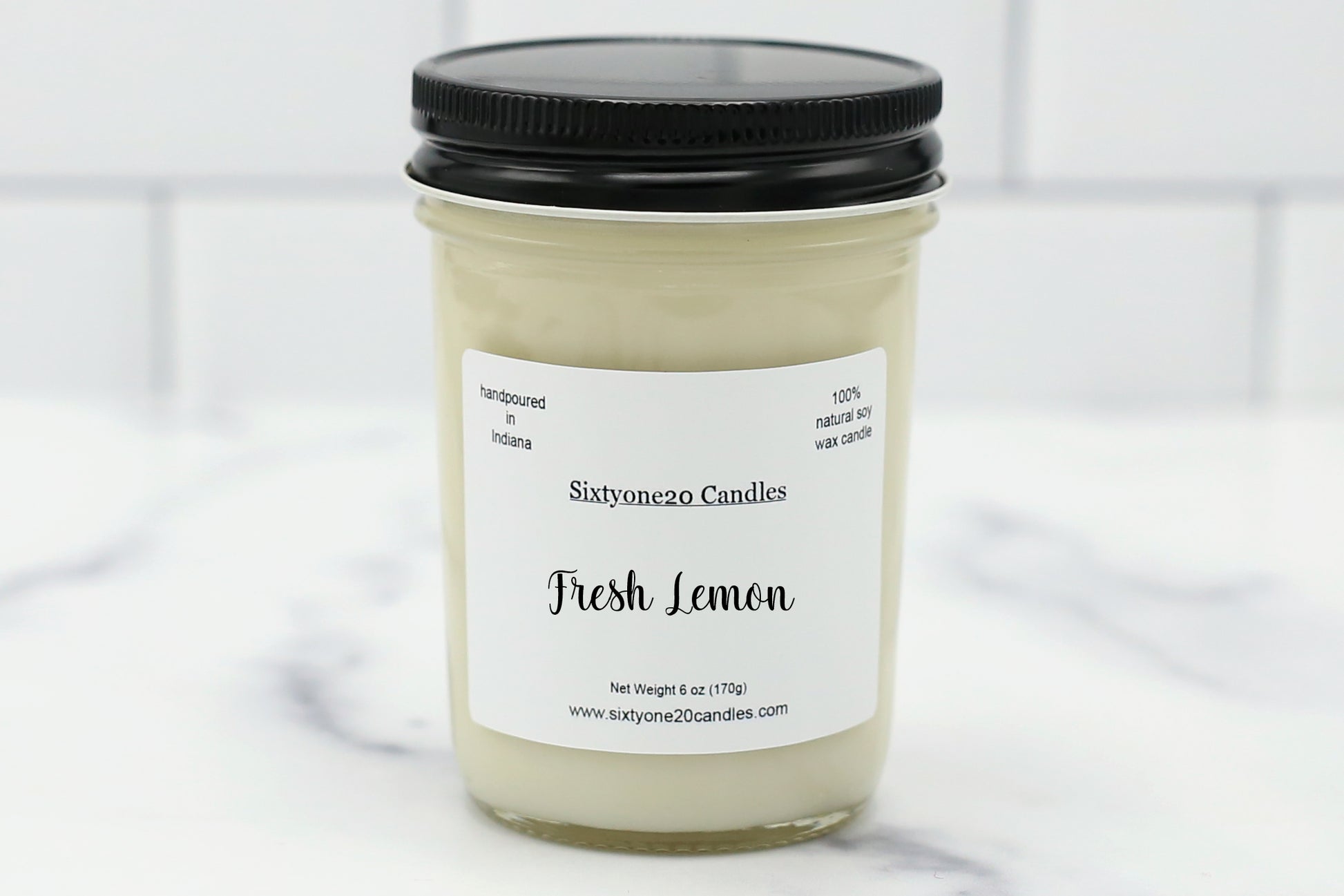 A hand-poured soy wax candle in a reusable glass jar, labeled "Fresh Lemon", surrounded by fresh lemons and citrus slices. The candle emits a bright, clean, and invigorating lemon fragrance with notes of zesty lemon, bergamot, and white musk. Perfect for refreshing any space with a crisp citrus scent.