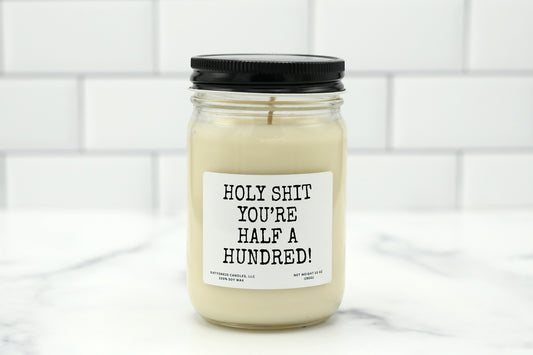 A 10 oz handmade soy wax candle with the label "Holy Shit, You’re Half a Hundred!"—a funny 50th birthday gift available in 10 custom scents.