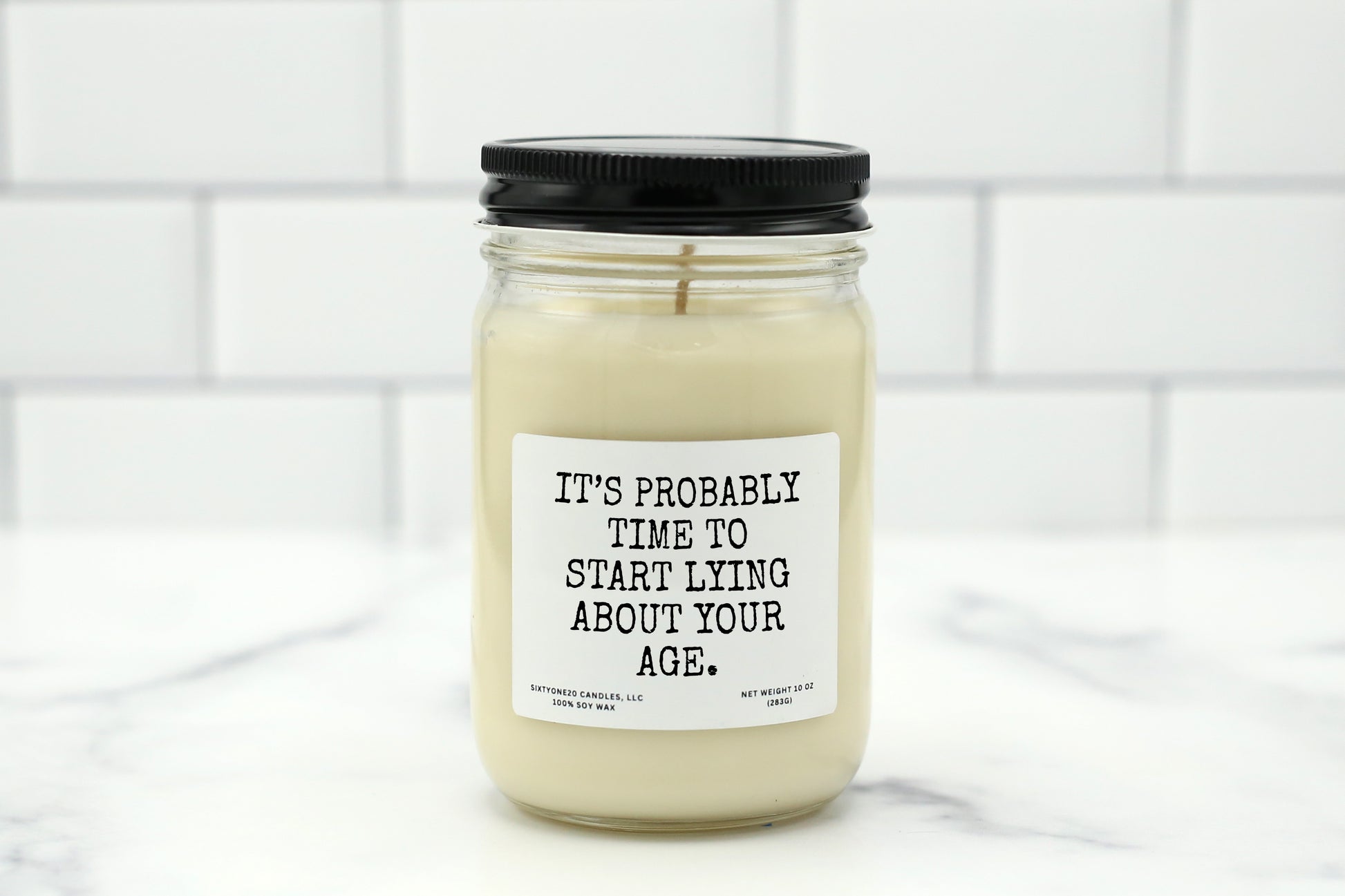 A 10 oz handmade soy wax candle with the label "It’s Probably Time to Start Lying About Your Age"—a funny birthday gift available in 10 custom scents.