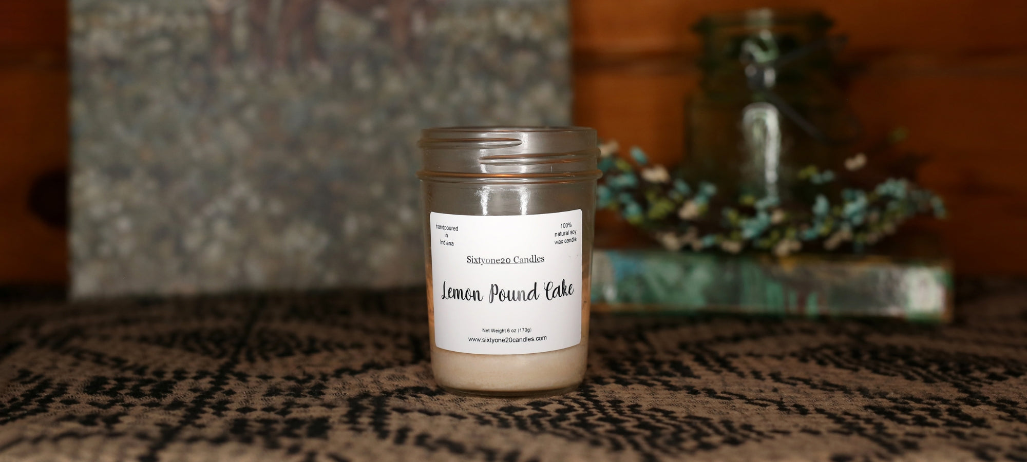 Candle jar labeled 'Lemon Pound Cake' on a textured surface with a blurred background