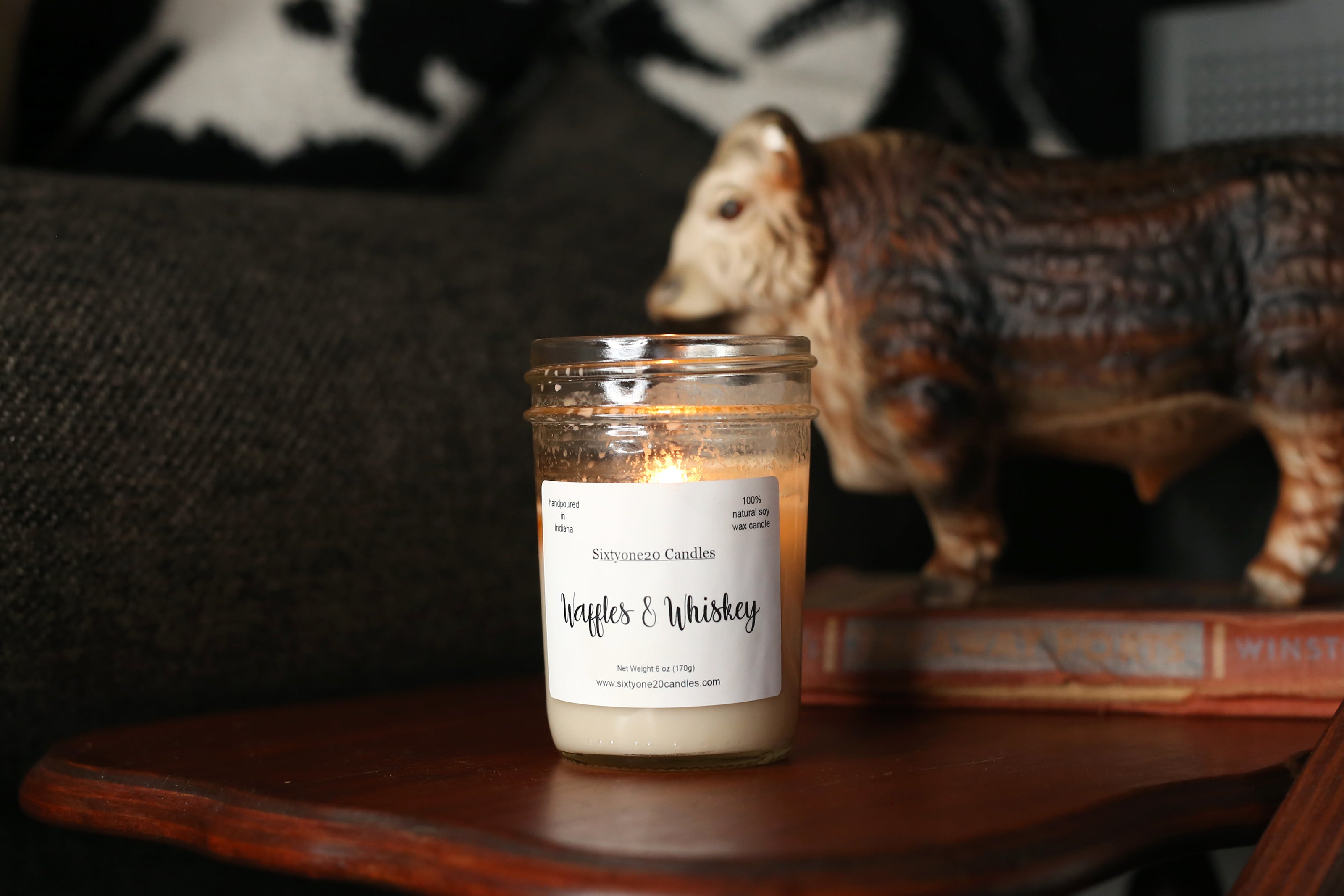 Candle labeled 'Waffles & Whiskey' on a wooden surface with a decorative animal figure in the background.